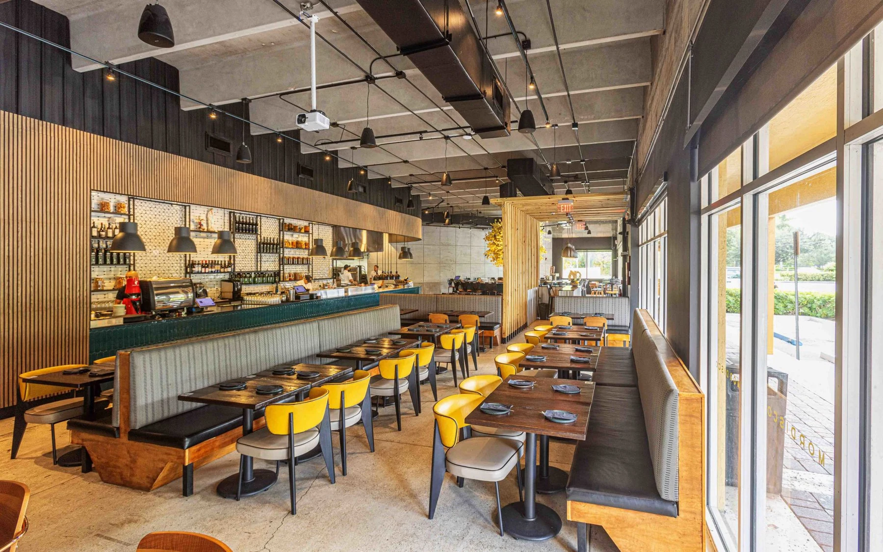 Mordisco's sunlit dining room with wooden tables, yellow chairs, upholstered booths and a teal-tiled counter